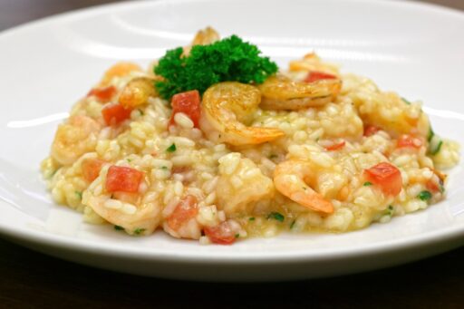 Um prato de risoto de camarão enfeitado com salsa, destacando-se pela sua aparência apetitosa e colorida.