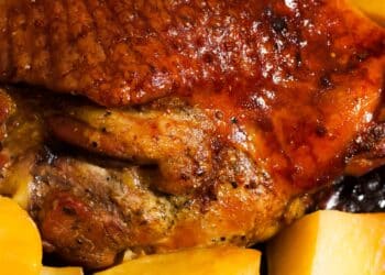 Um prato de carne ao forno dourada e suculenta acompanhada de batatas assadas amarelas e macias.